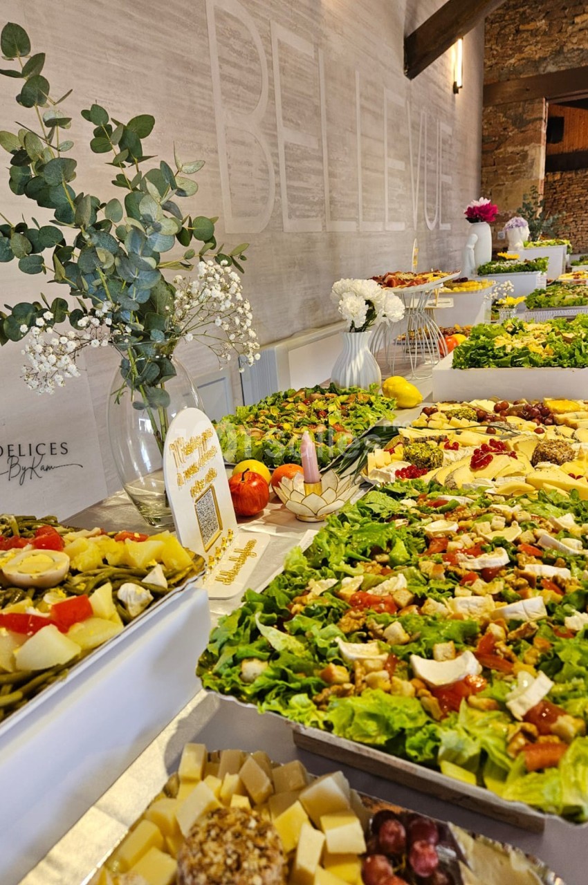 Buffet varié avec salades, fromages, fruits et décorations florales dans une salle lumineuse en pierre apparente.