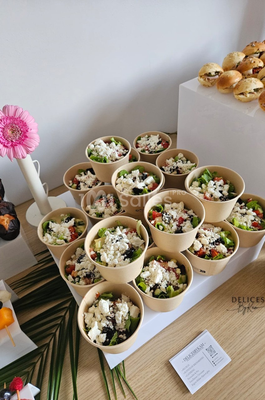 Salades colorées en portions individuelles dans des bols en carton, accompagnées de mini-burgers et brochettes de fruits.