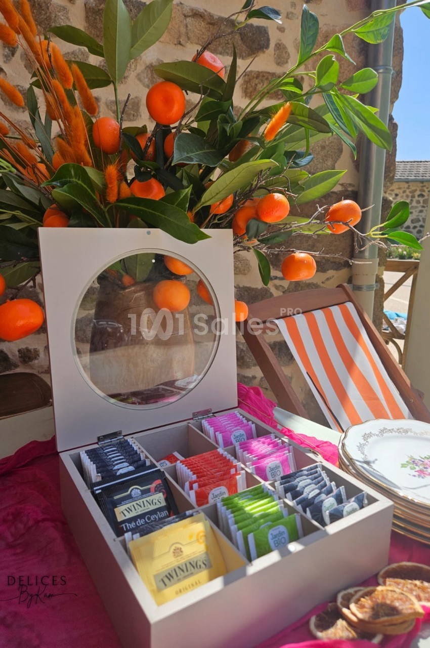 Boîte ouverte contenant des sachets de thé variés, posée sur une table décorée avec des branches d'oranges et de la…