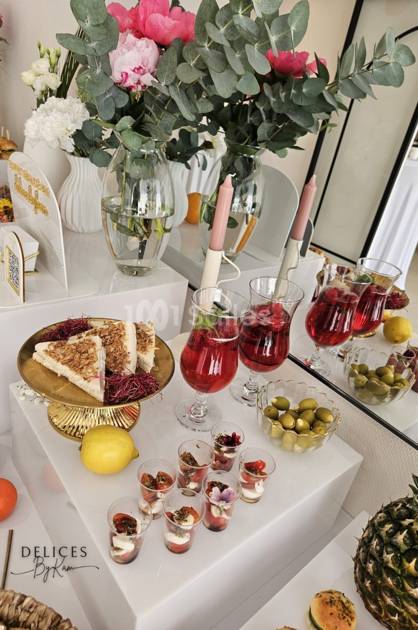 Table garnie de desserts, verrines, boissons rouges, olives, fruits et décorations florales dans un cadre élégant.