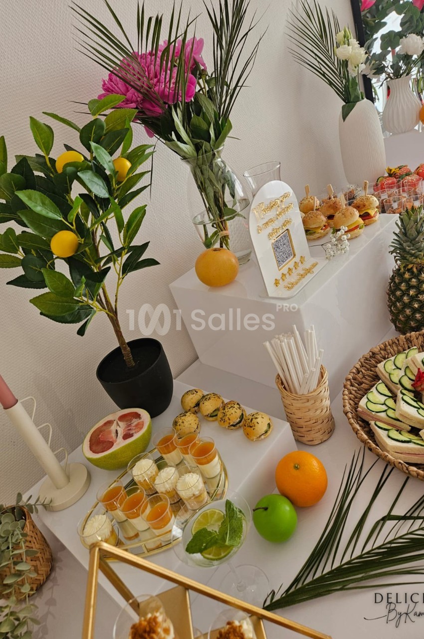 Buffet décoré avec des fleurs, fruits frais, verrines, mini-burgers et desserts, présenté sur une table élégante.