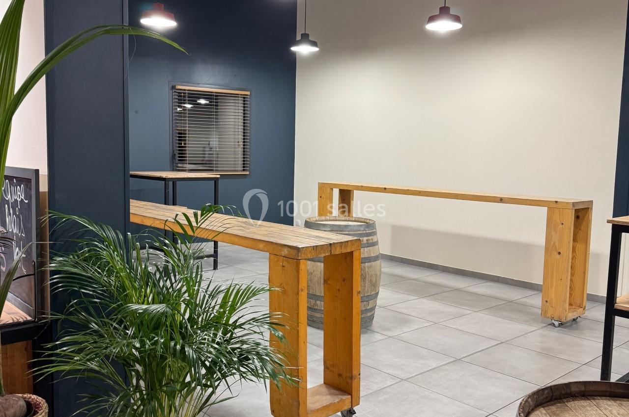Salle moderne avec murs bleu foncé, tables en bois sur roulettes, tonneaux décoratifs et plantes en pot.