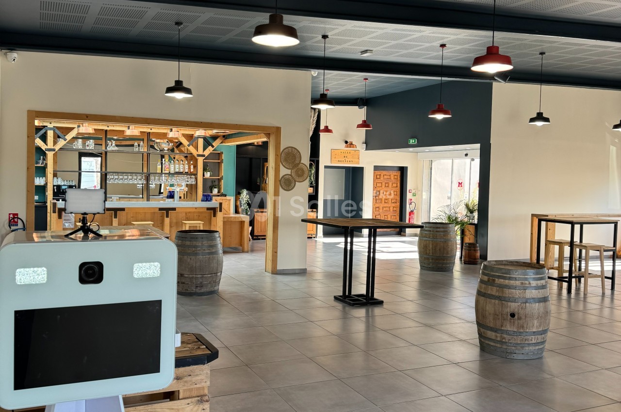Salle lumineuse avec bar en bois, tables hautes, tonneaux décoratifs et un photobooth au premier plan.