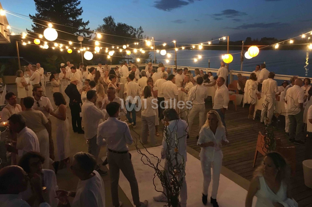 Groupe de personnes en tenue blanche lors d'une soirée en plein air, éclairée par des guirlandes lumineuses, près d'un plan…