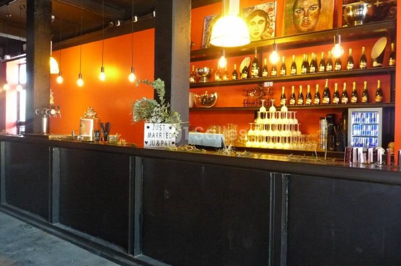 Bar avec comptoir noir, décorations murales colorées, étagères de bouteilles et présentoir de coupes de champagne.