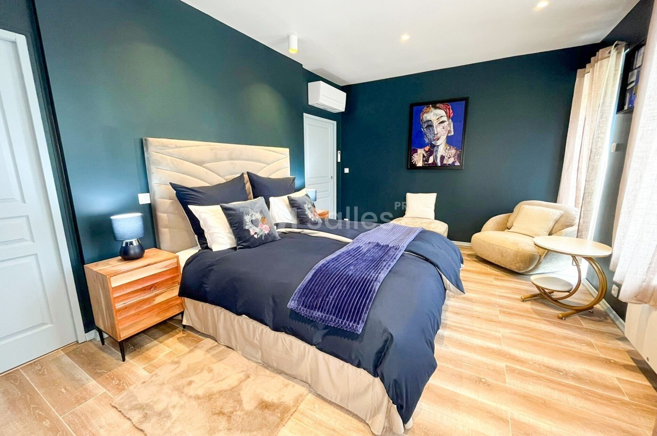 Chambre moderne avec murs bleu foncé, lit double, fauteuil beige, parquet clair et éclairage intégré.