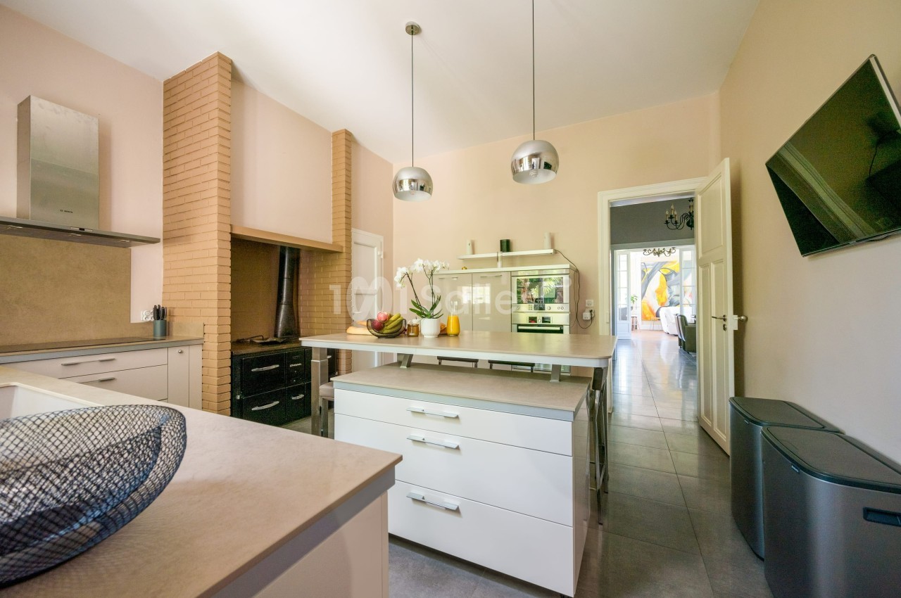 Cuisine moderne avec îlot central, meubles blancs, électroménagers intégrés, et lumière naturelle entrant par une porte…