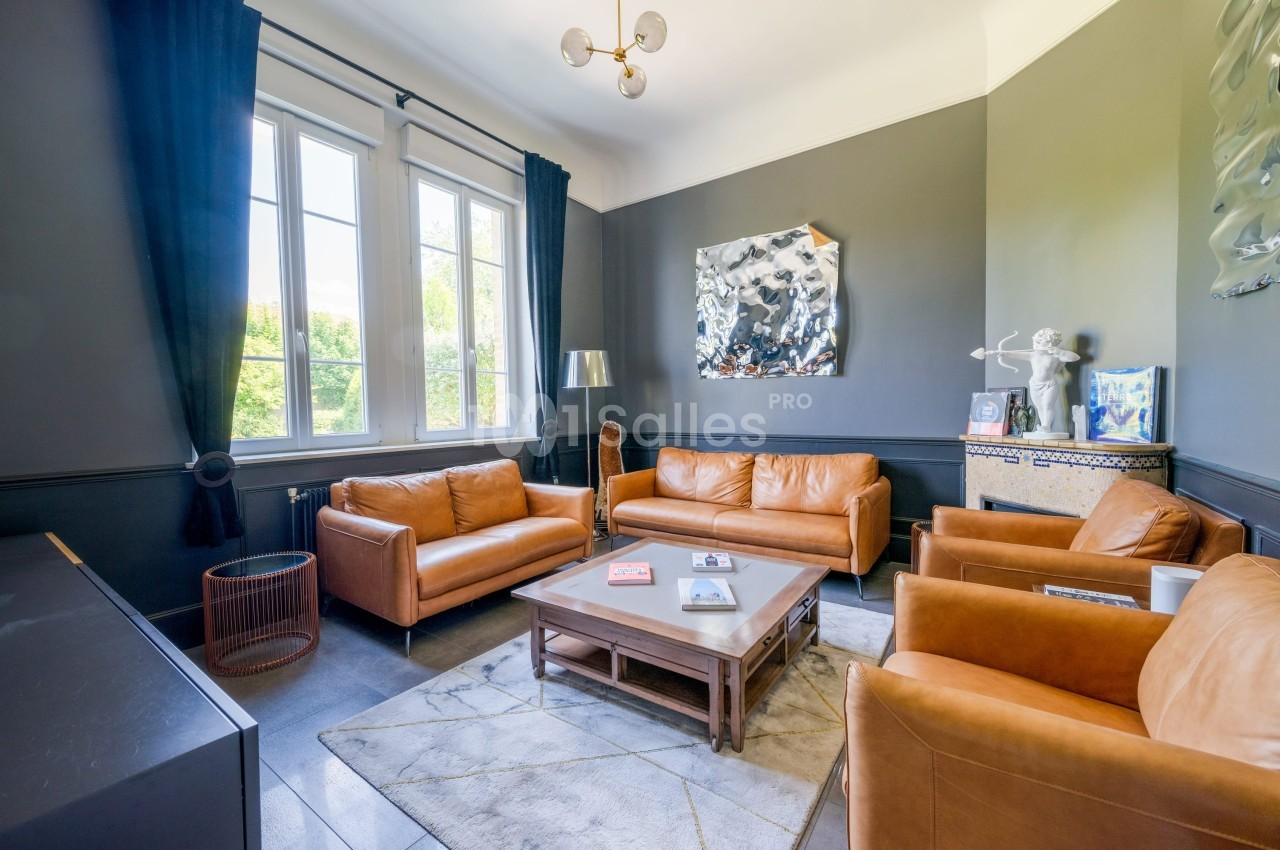 Salon lumineux avec murs sombres, mobilier en cuir marron, table basse en bois et grande fenêtre donnant sur un jardin.