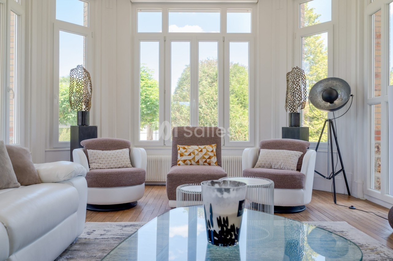 Salon lumineux avec fauteuils modernes, grandes fenêtres donnant sur un jardin et décoration contemporaine.