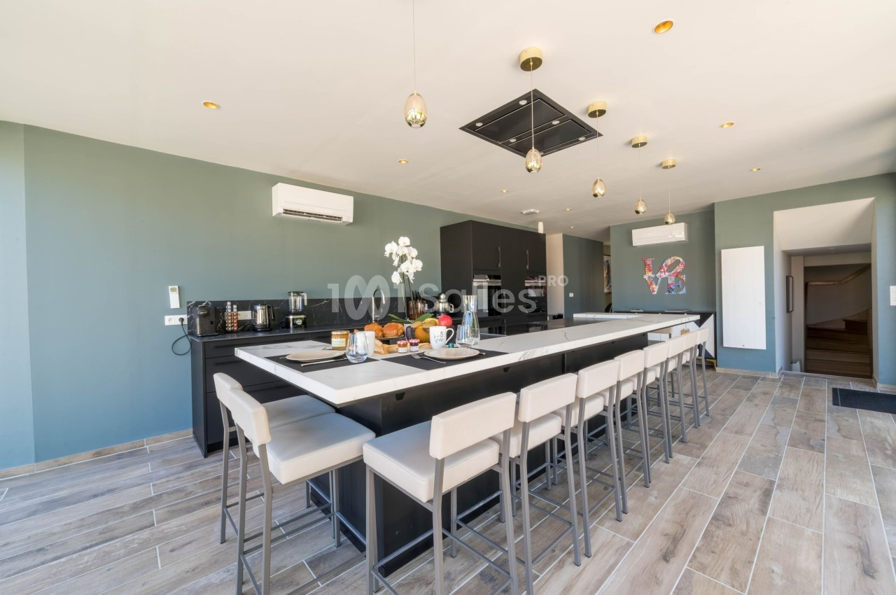 Cuisine moderne avec un grand îlot central, chaises hautes, plan de travail noir et éclairage suspendu.