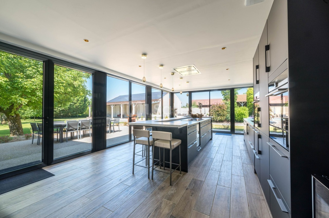 Cuisine moderne avec îlot central, grandes baies vitrées donnant sur un jardin et terrasse extérieure.