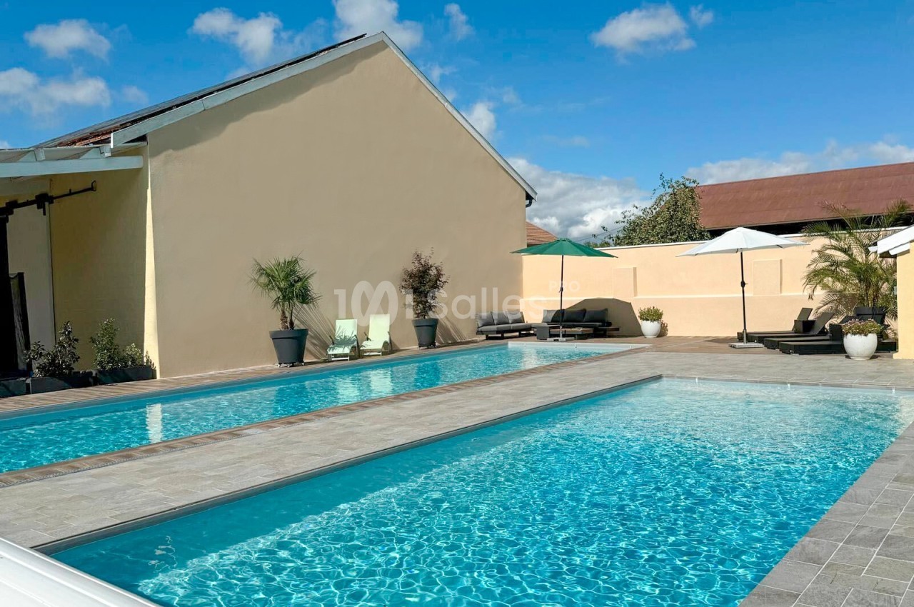 Deux piscines extérieures entourées de transats, parasols et végétation, dans une cour ensoleillée.