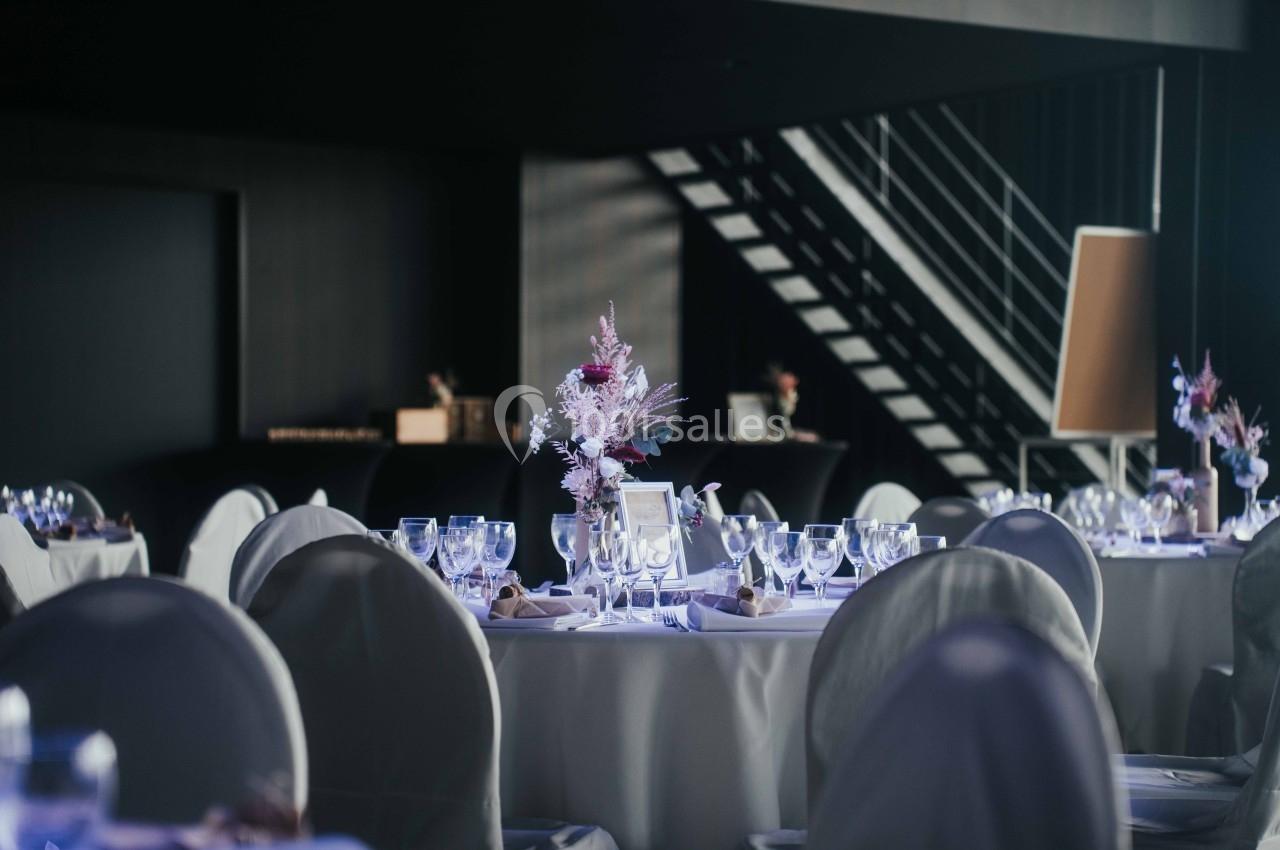 Salle de réception élégante avec tables dressées, nappes blanches, verres et centre de table floral.
