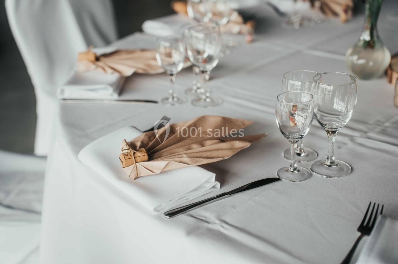 Table dressée avec nappes blanches, serviettes pliées en éventail, verres à pied et couverts disposés.