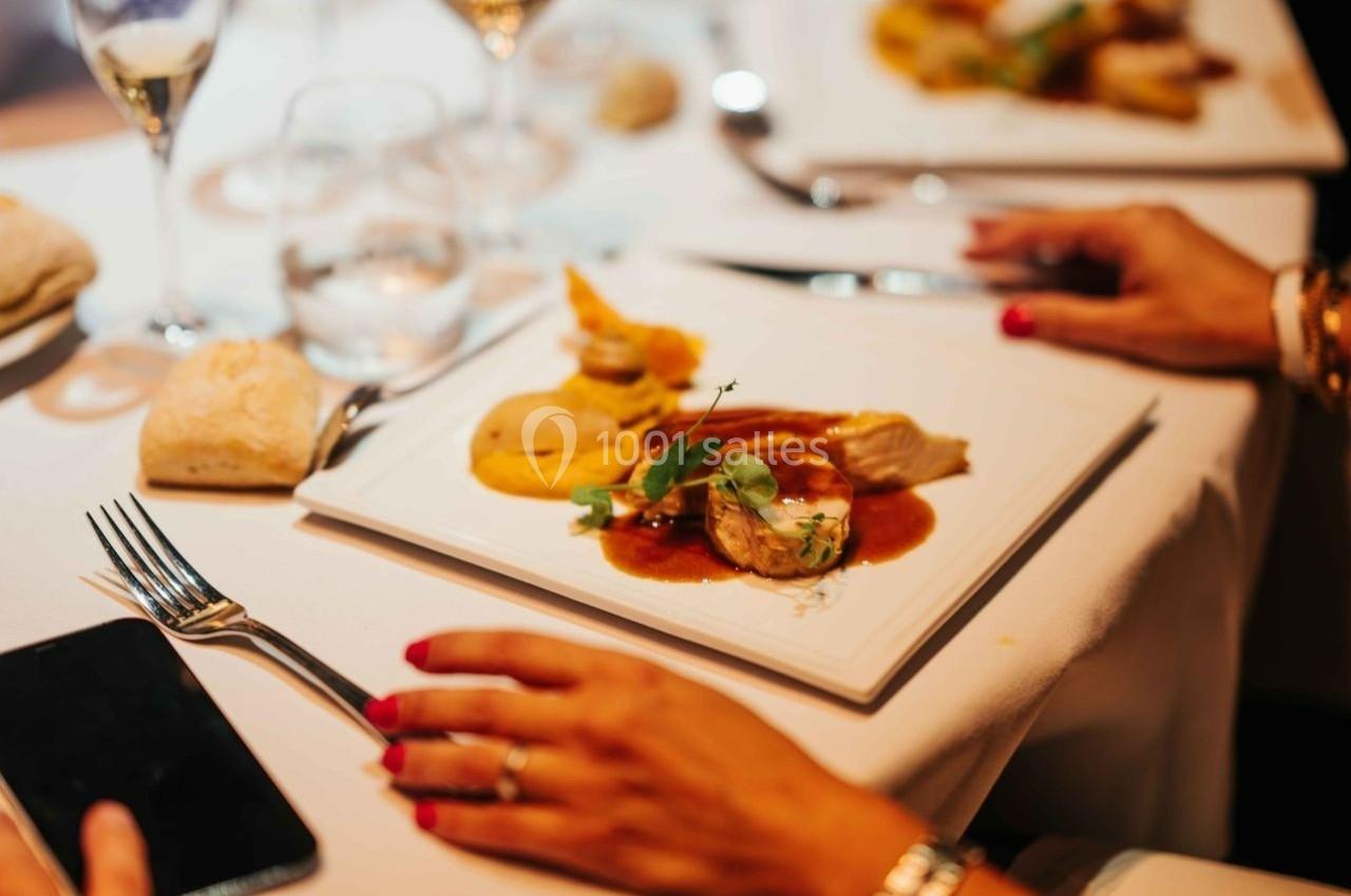 Assiette gastronomique avec viande, purée et sauce, servie sur une table élégante avec couverts et verre à vin.