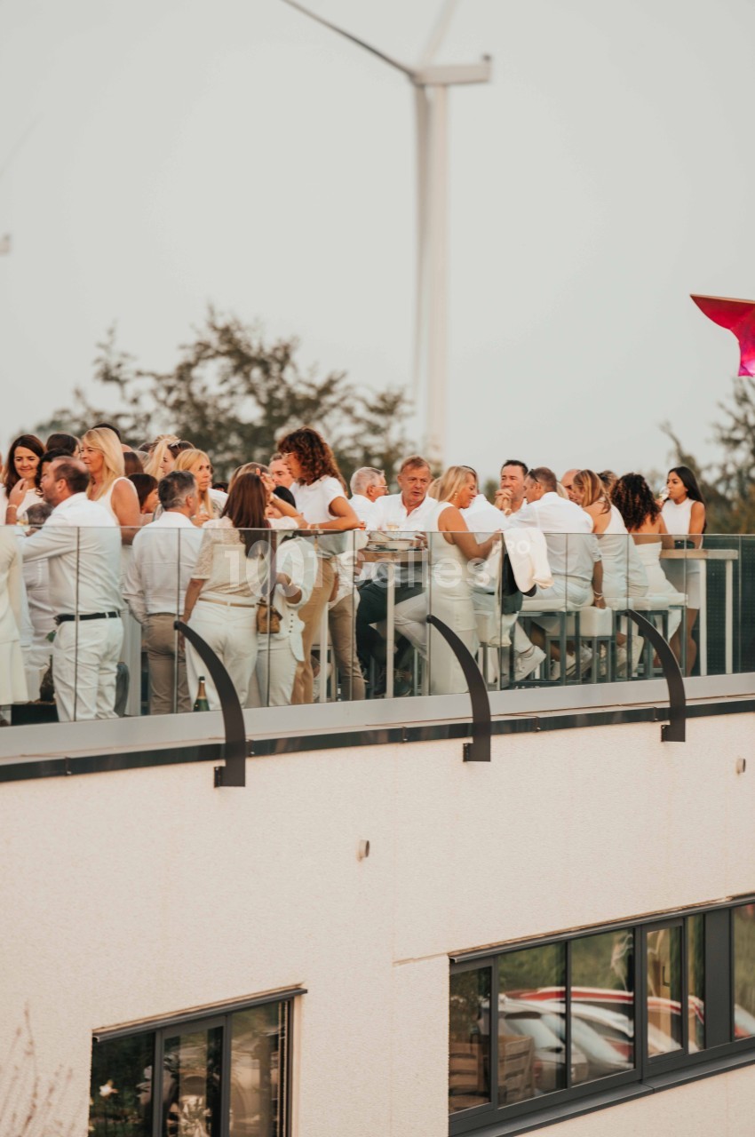 Groupe de personnes en tenue blanche réunies sur une terrasse en hauteur, avec des arbres et une éolienne en arrière-plan.