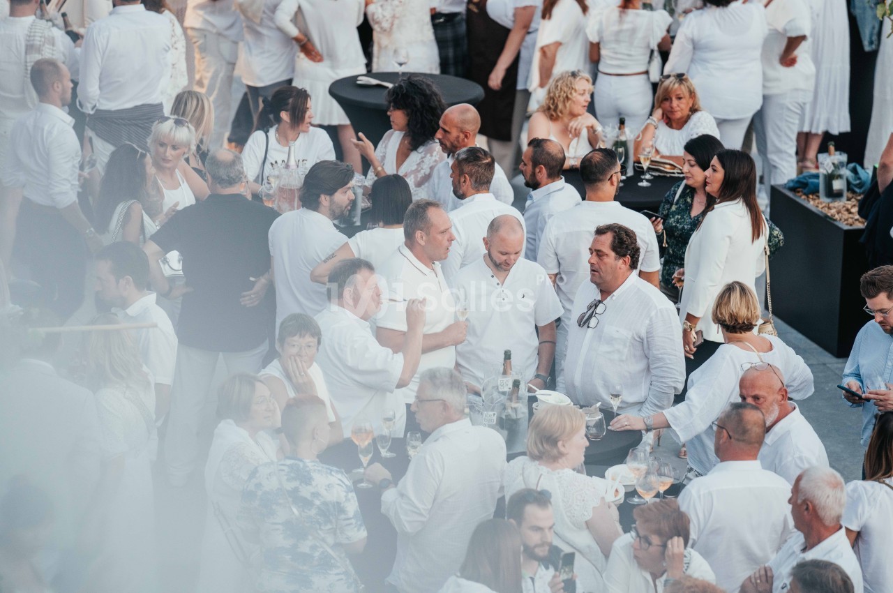 Groupe de personnes vêtues de blanc discutant et partageant un moment convivial lors d'un événement en plein air.