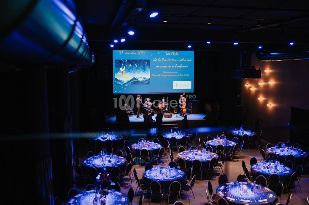 Salle de réception avec tables dressées et un groupe de musiciens jouant sur scène devant un écran projeté.