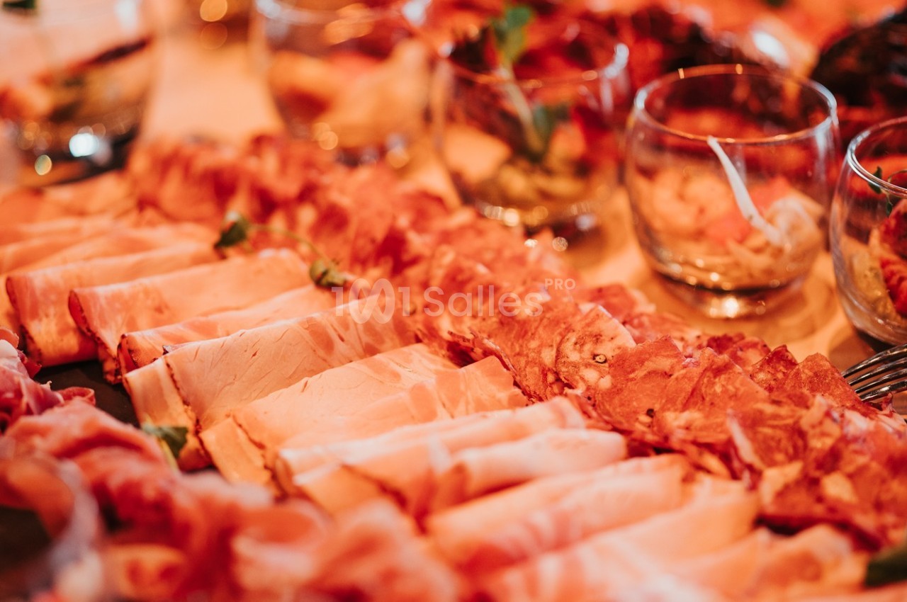 Assortiment de charcuteries disposées sur une table, accompagné de verrines en arrière-plan.