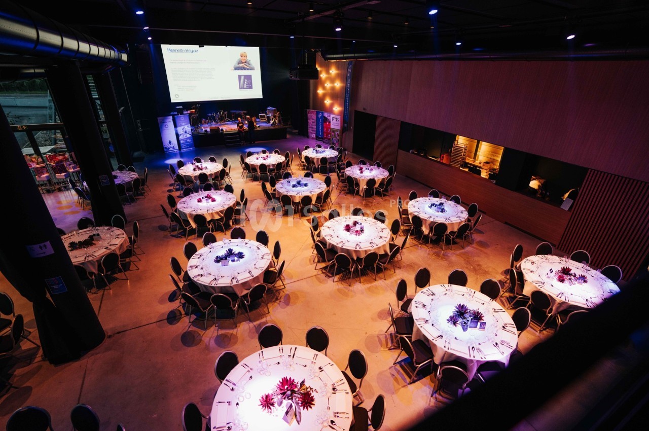 Salle de réception avec des tables rondes dressées, éclairage tamisé et écran de projection en arrière-plan.