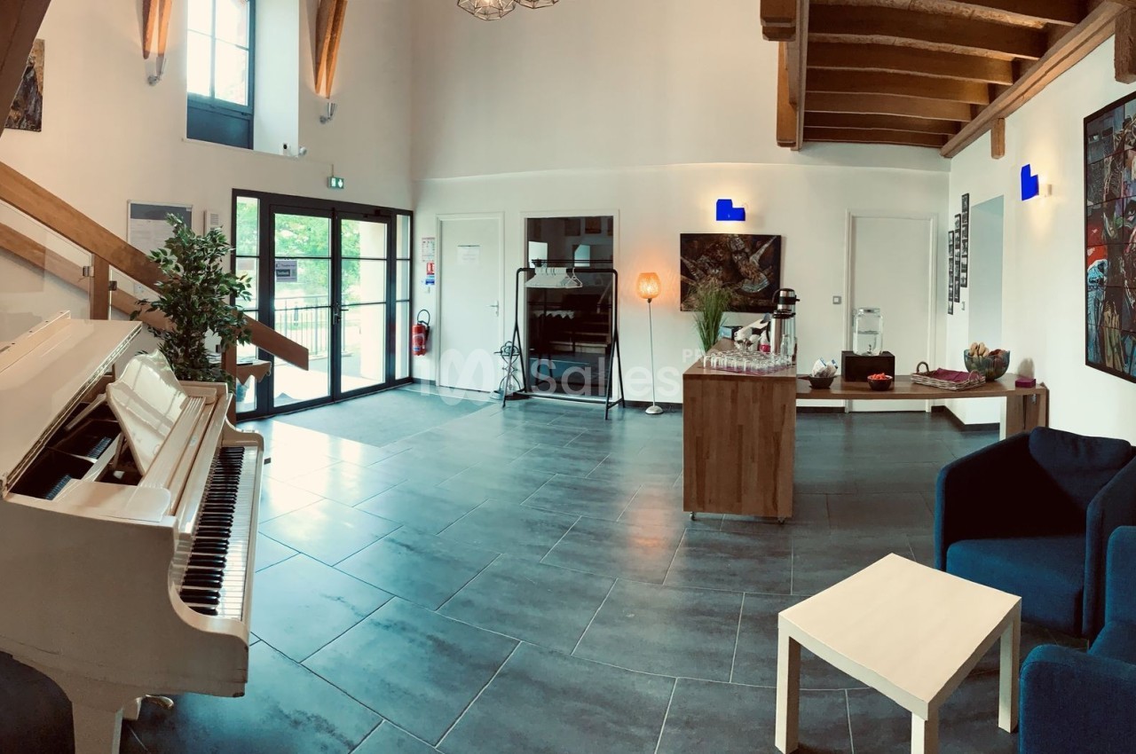 Intérieur lumineux avec un piano blanc, des fauteuils bleus, un escalier en bois et des œuvres d'art accrochées aux murs.