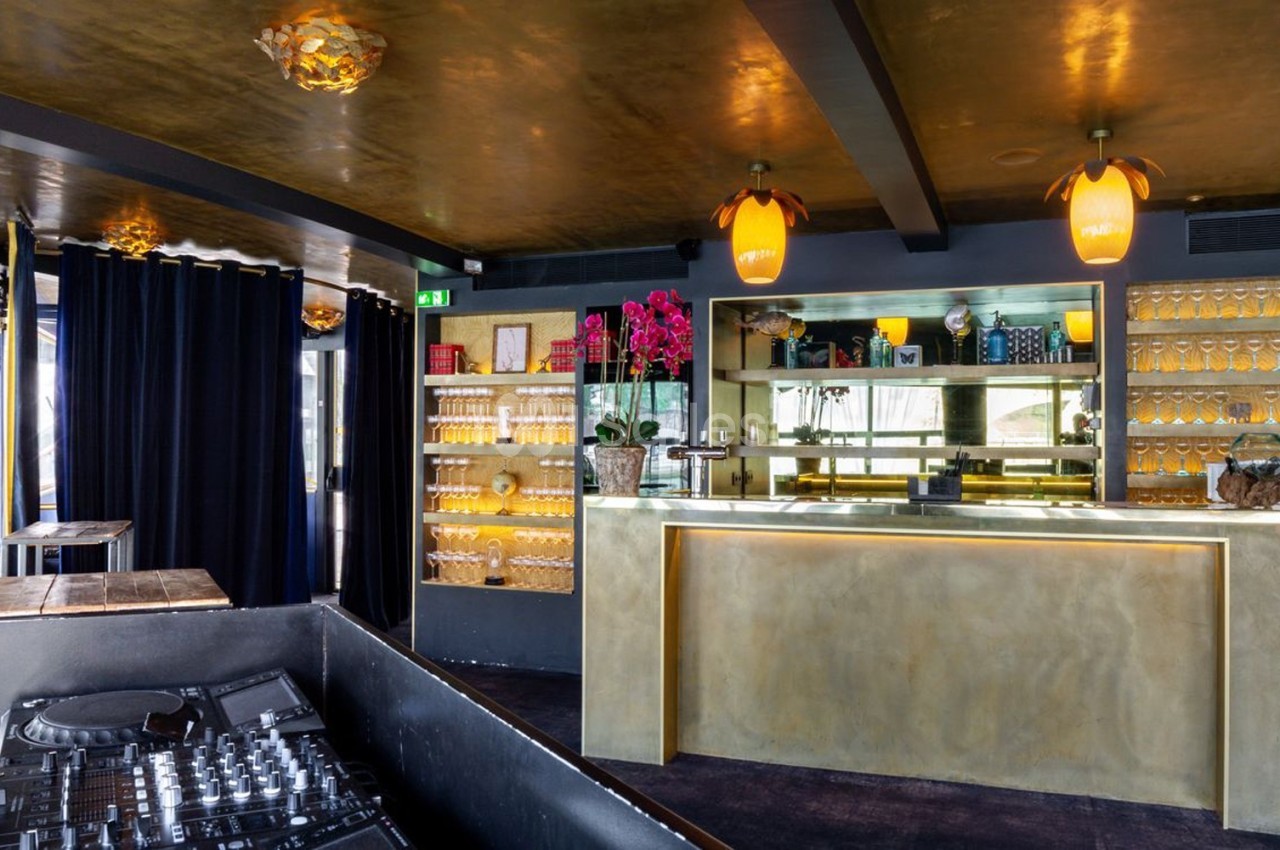 Bar moderne avec comptoir doré, étagères garnies de verres et décorations, éclairage chaleureux et table de mixage au…