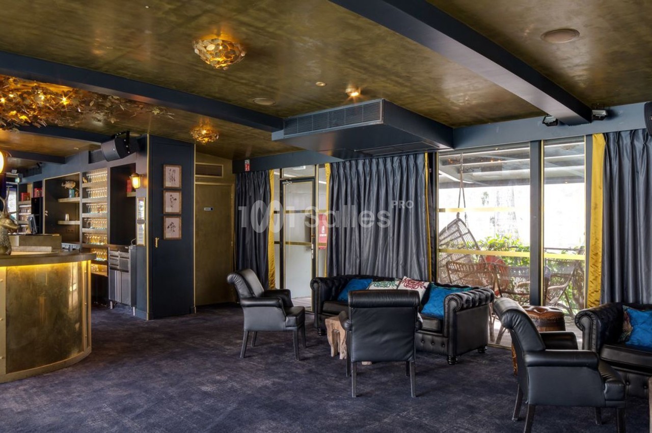 Salon élégant avec fauteuils en cuir, bar doré, rideaux sombres et grandes fenêtres donnant sur une terrasse.