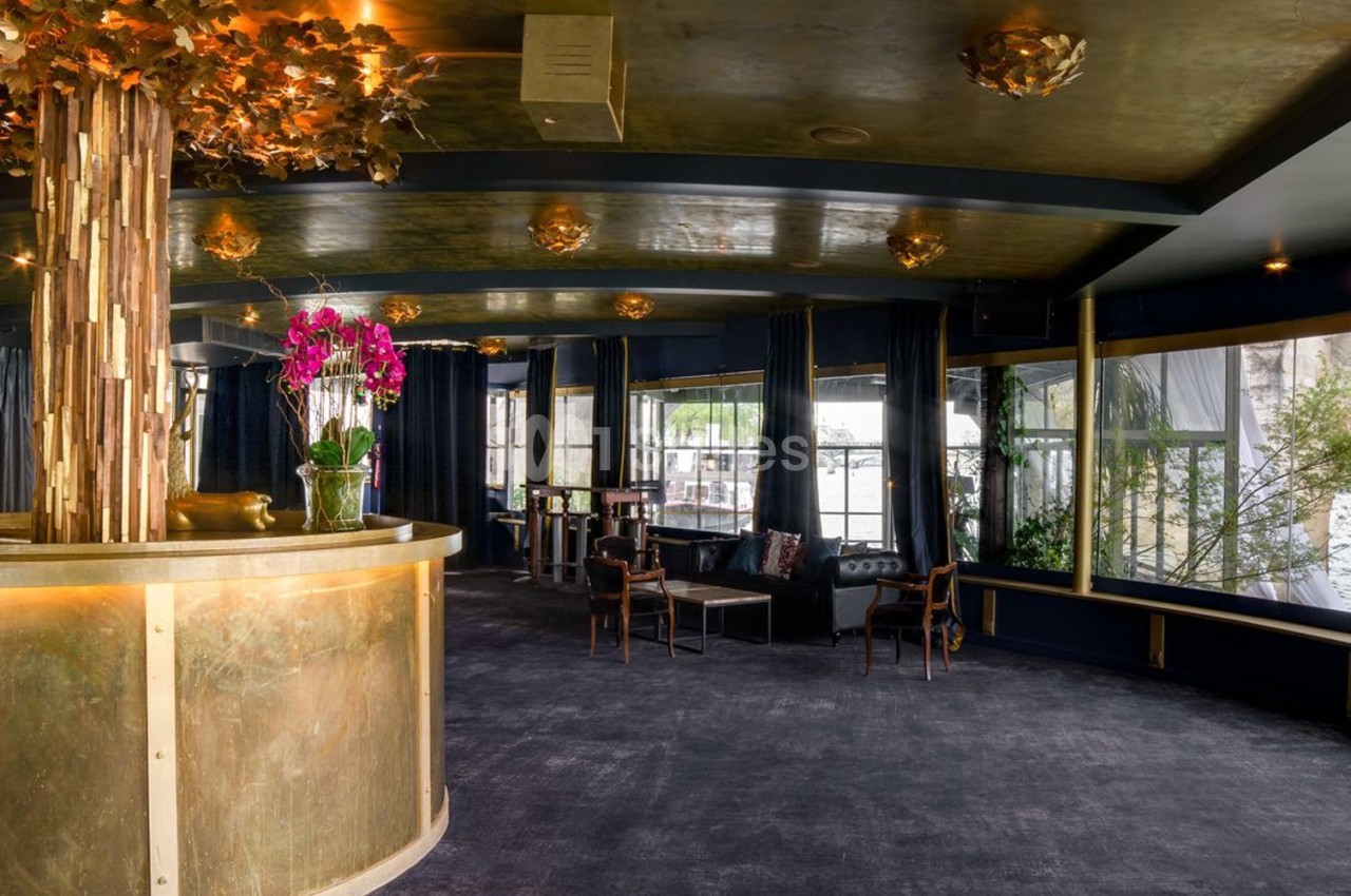 Intérieur d'un espace élégant avec un comptoir doré, des orchidées et de grandes baies vitrées donnant sur l'extérieur.