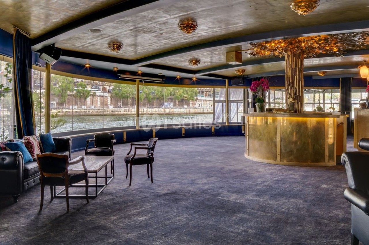 Salle élégante avec grandes baies vitrées, mobilier chic et comptoir doré, offrant une vue sur un canal.