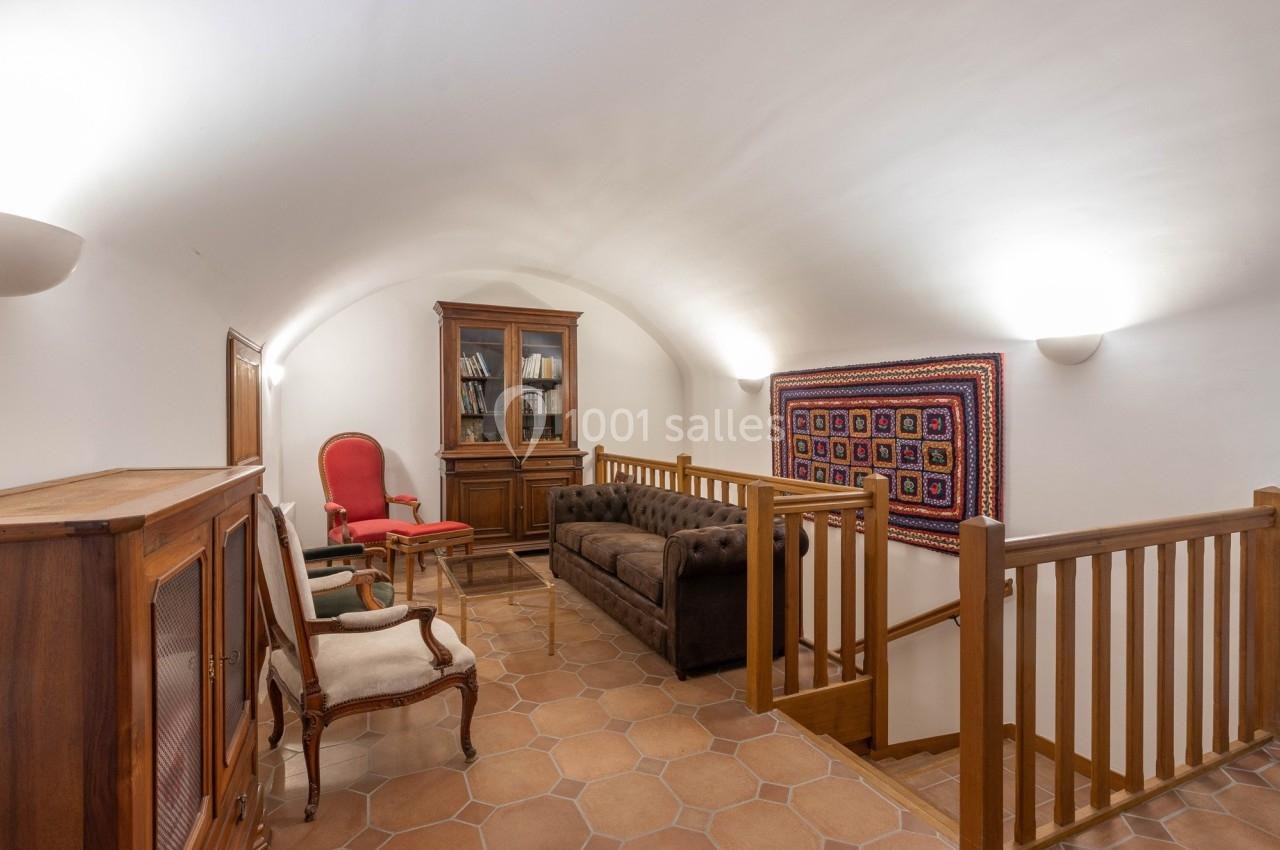 Salon avec plafond voûté, canapé en cuir, fauteuils, bibliothèque en bois et tapis mural coloré.