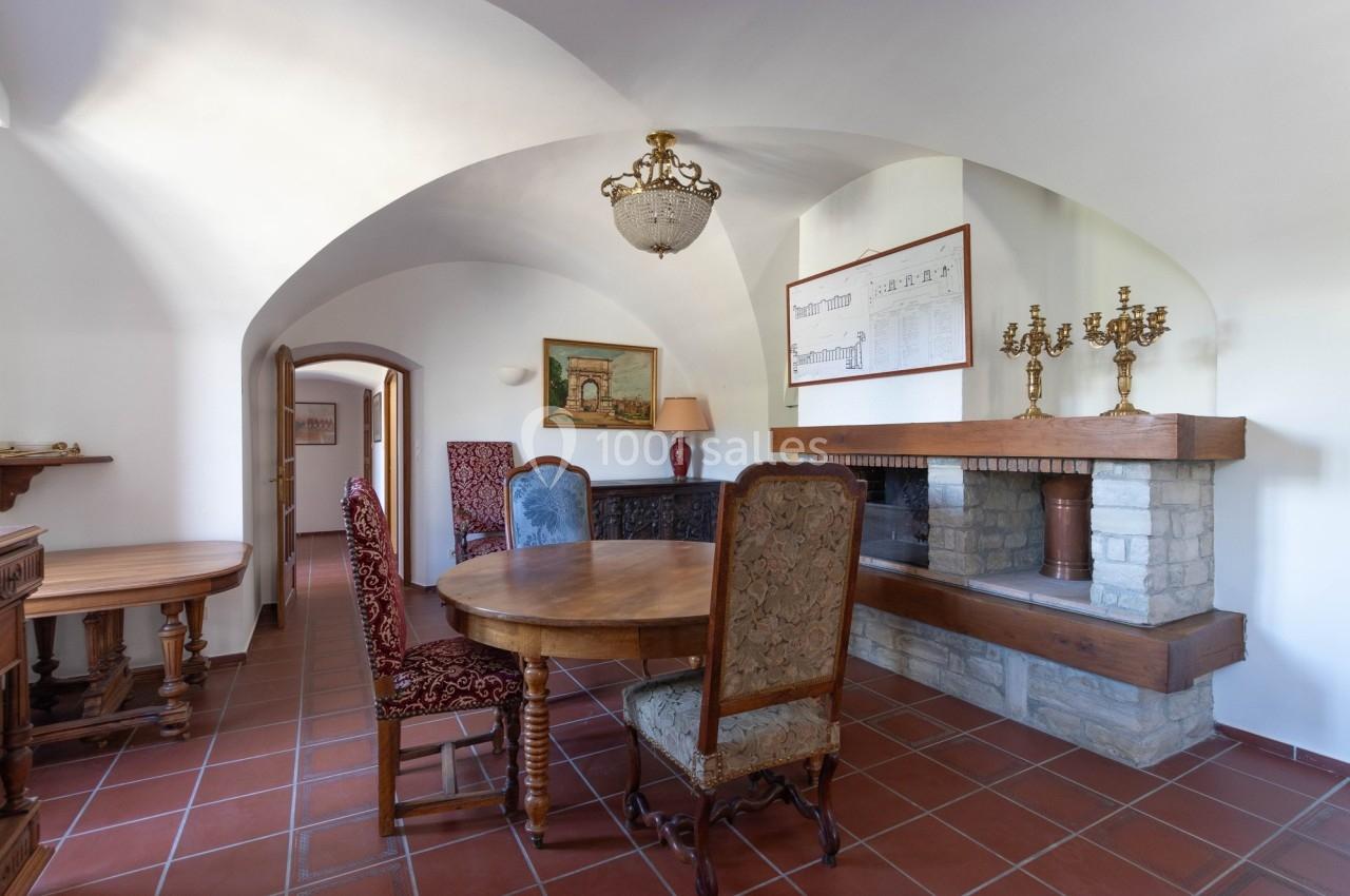 Salle à manger avec table ronde en bois, chaises assorties, cheminée en pierre et décoration murale.