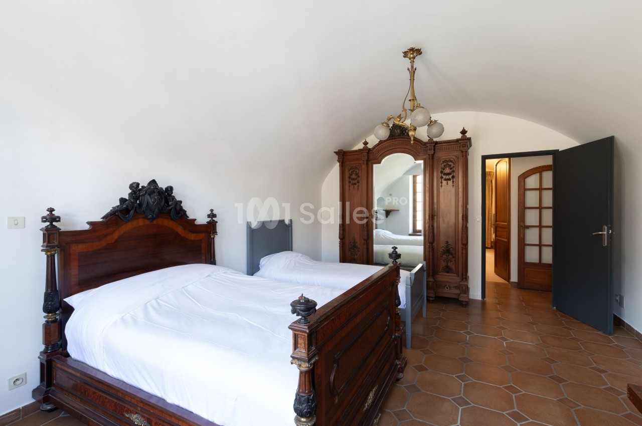 Chambre avec lit ancien en bois sculpté, armoire assortie, sol en carrelage et porte ouverte sur une autre pièce.