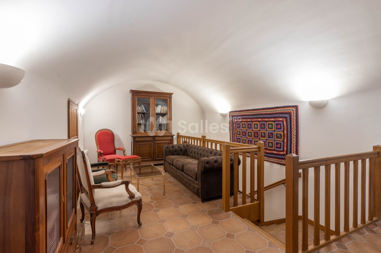 Salon avec plafond voûté, canapé en cuir, fauteuils, bibliothèque en bois et tapis mural coloré.