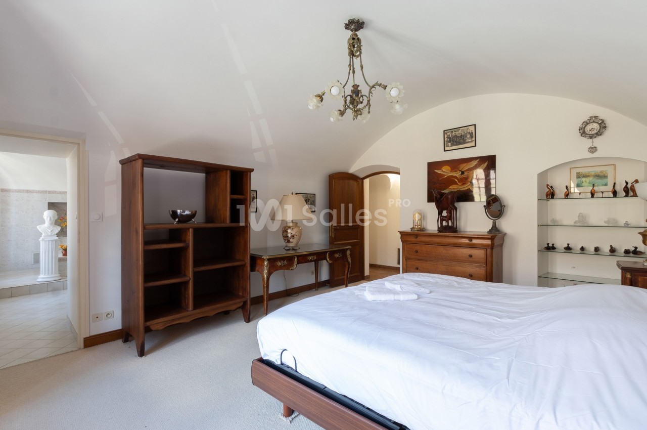 Chambre lumineuse avec lit double, mobilier en bois, étagères, et vue sur un couloir menant à une autre pièce.