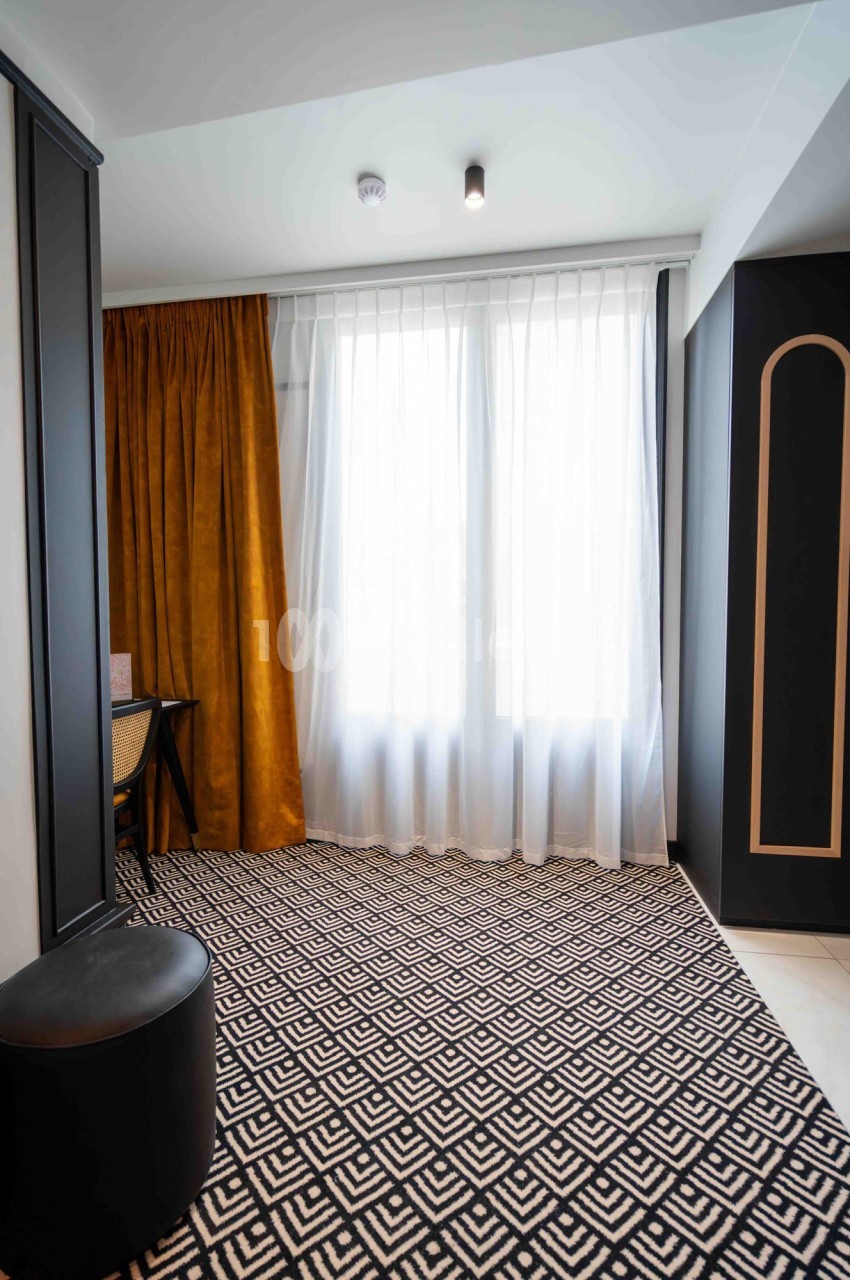 Rideaux dorés et voilages blancs encadrant une fenêtre, avec un tapis à motifs géométriques noir et blanc au sol.