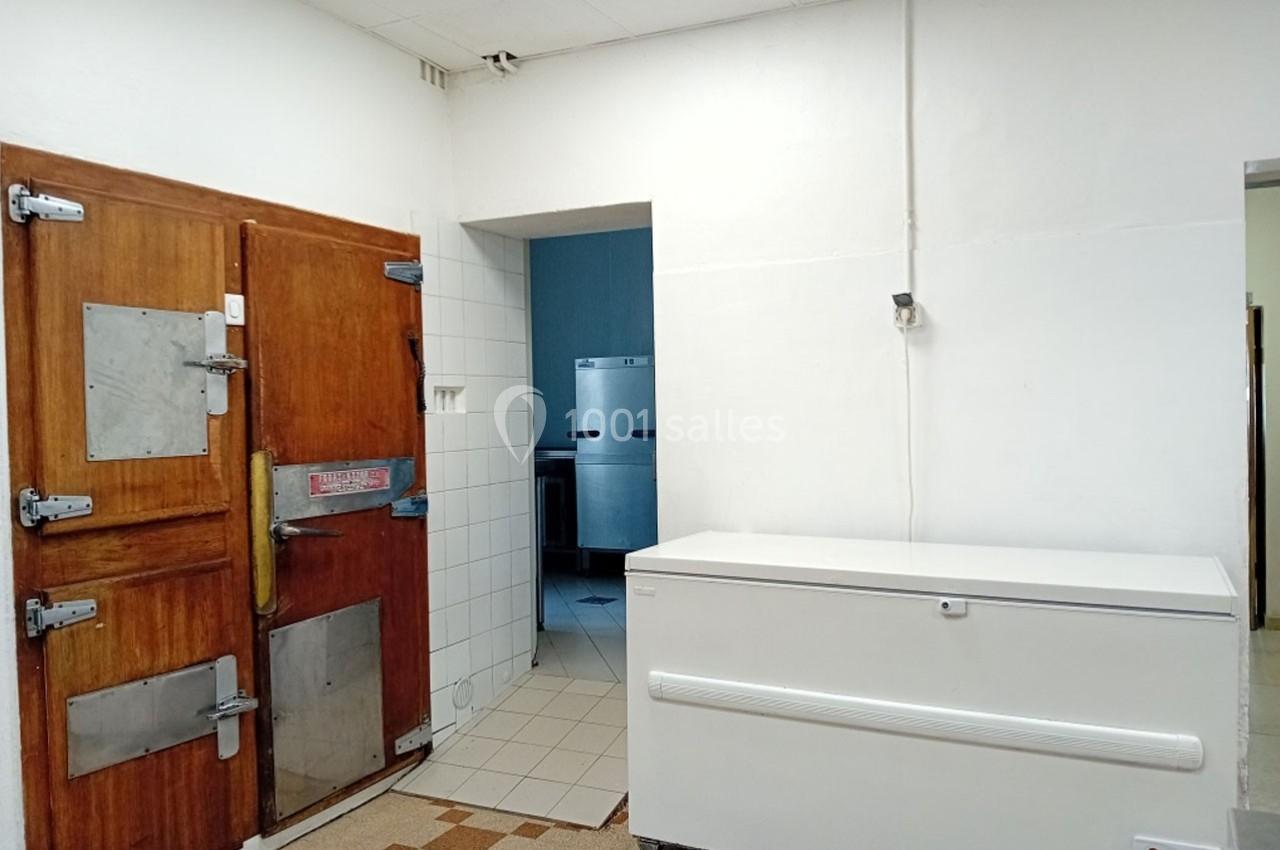 Chambre froide avec porte en bois et congélateur blanc dans une pièce carrelée à usage professionnel.