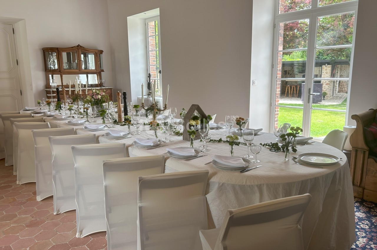 Table dressée pour un repas, avec nappes blanches, vaisselle élégante et décor floral, dans une salle lumineuse.