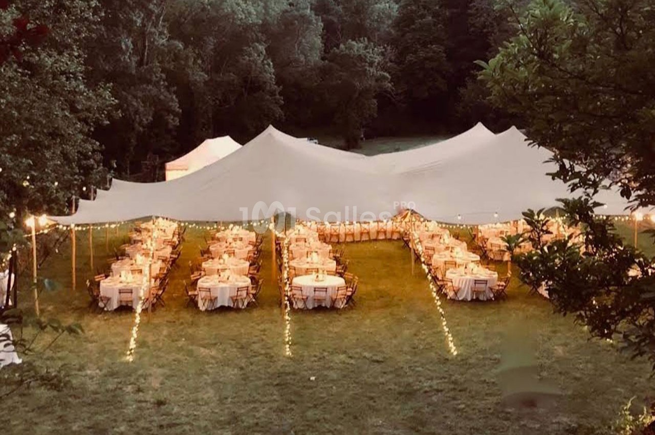 Grande tente blanche installée dans un espace extérieur, abritant des tables rondes décorées pour un événement festif.