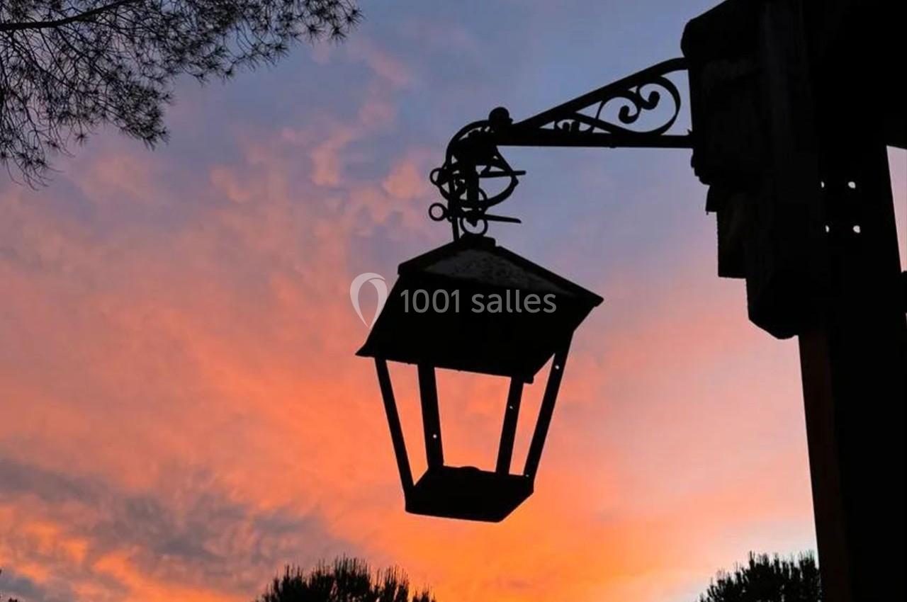 Lanterne suspendue en fer forgé silhouettée devant un ciel coloré au coucher du soleil.