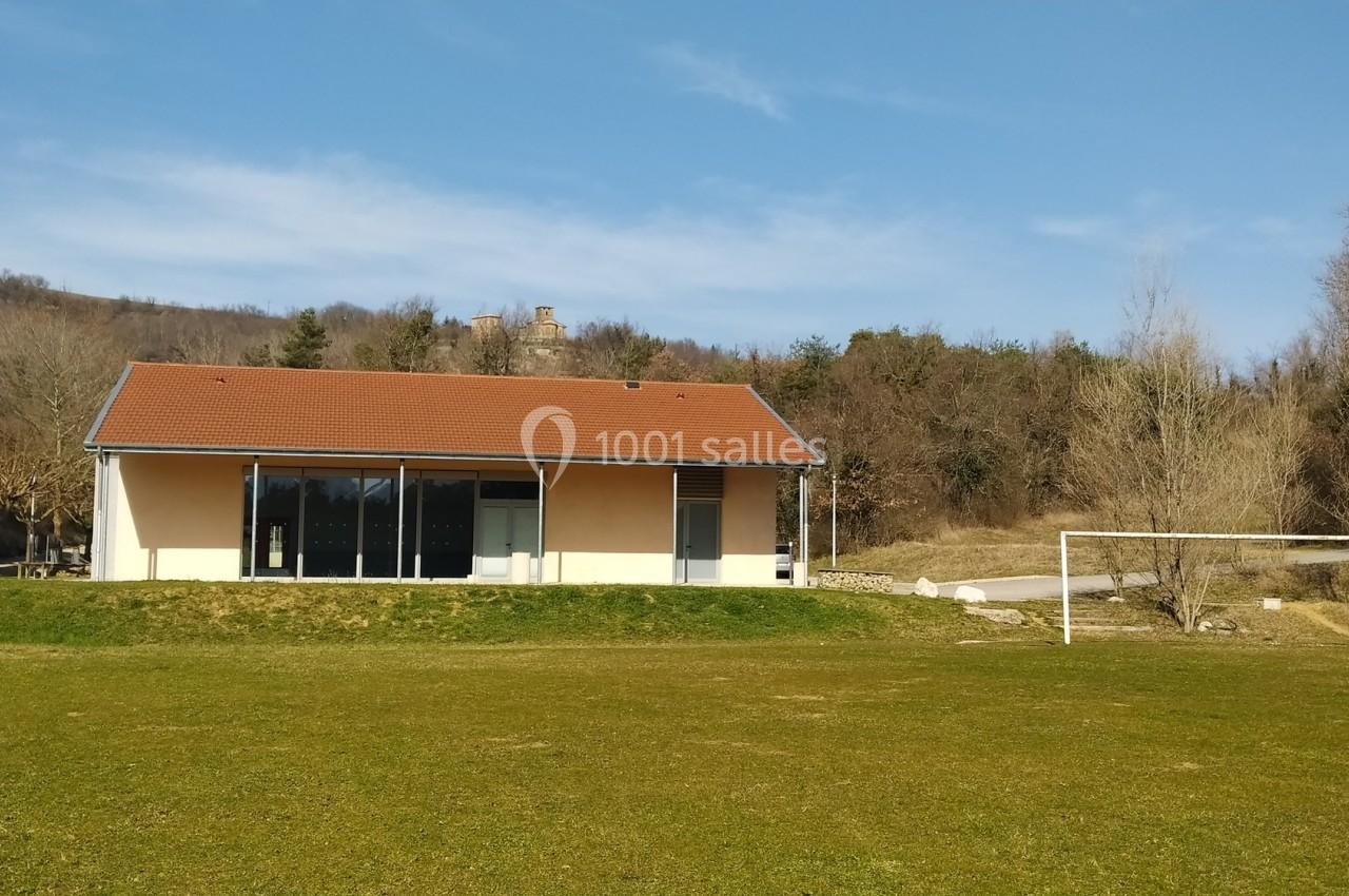 Bâtiment moderne à toit rouge entouré de nature, avec un terrain de sport et des arbres en arrière-plan.