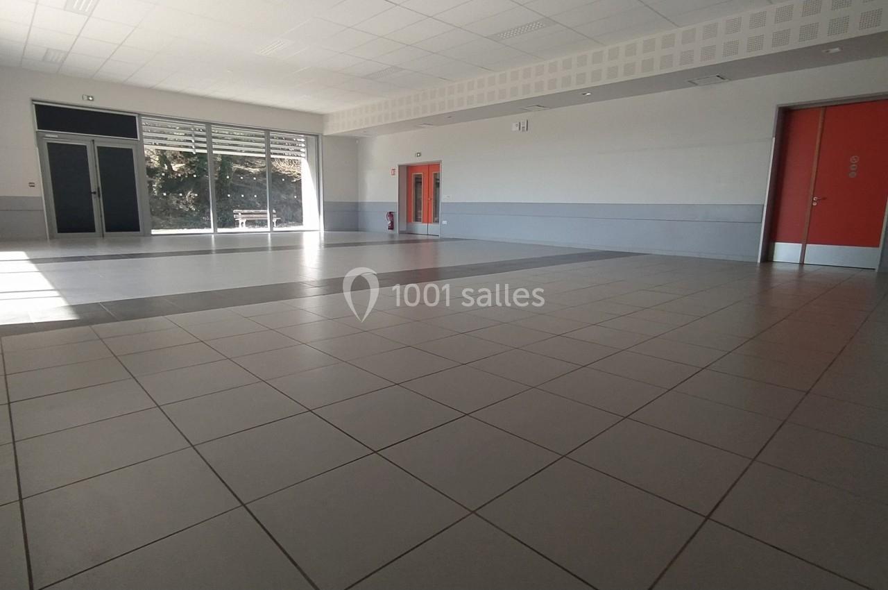 Salle vide avec sol carrelé, murs clairs, deux portes rouges et une grande baie vitrée laissant entrer la lumière naturelle.