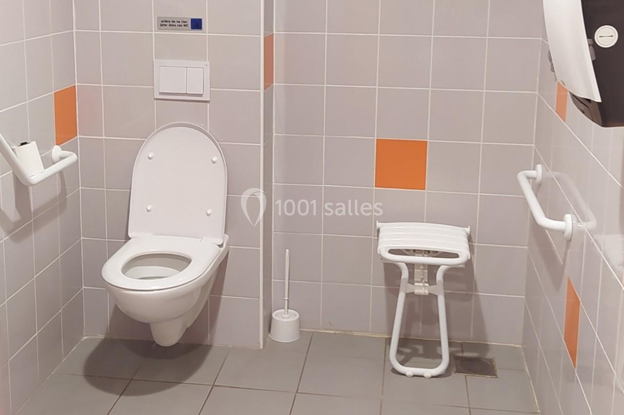 Toilettes accessibles avec barre d'appui, siège pliant et carrelage gris et orange.