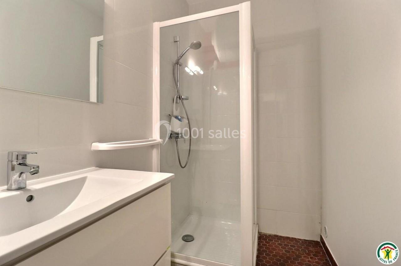 Douche moderne avec paroi vitrée, pommeau mural et lavabo blanc dans une salle de bain aux murs clairs.