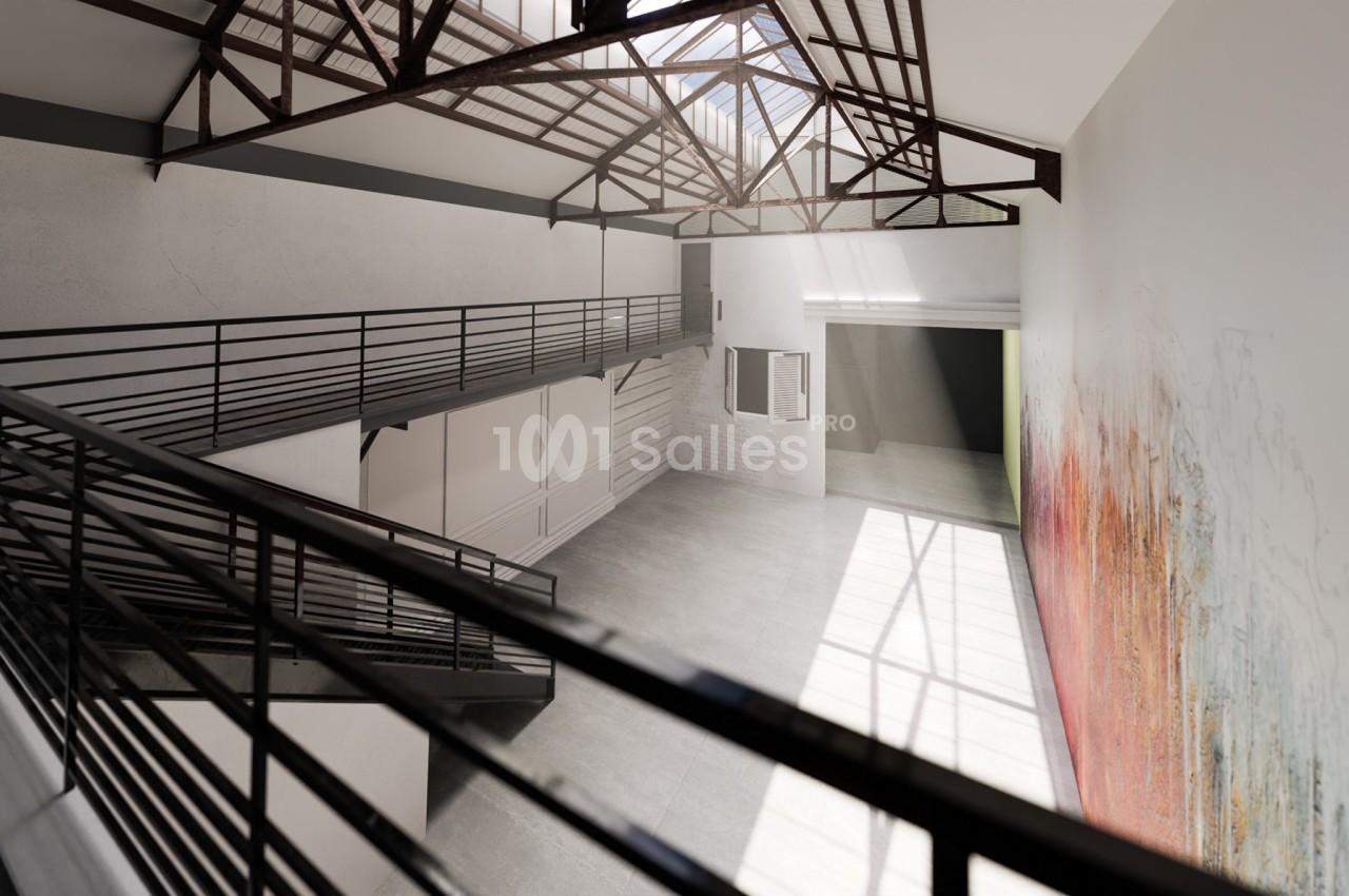 Intérieur d'un grand espace lumineux avec mezzanine, structure métallique apparente et mur décoré de motifs colorés.