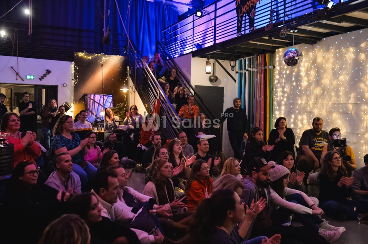 Un public assis applaudit dans une salle décorée de guirlandes lumineuses et d'une boule disco.