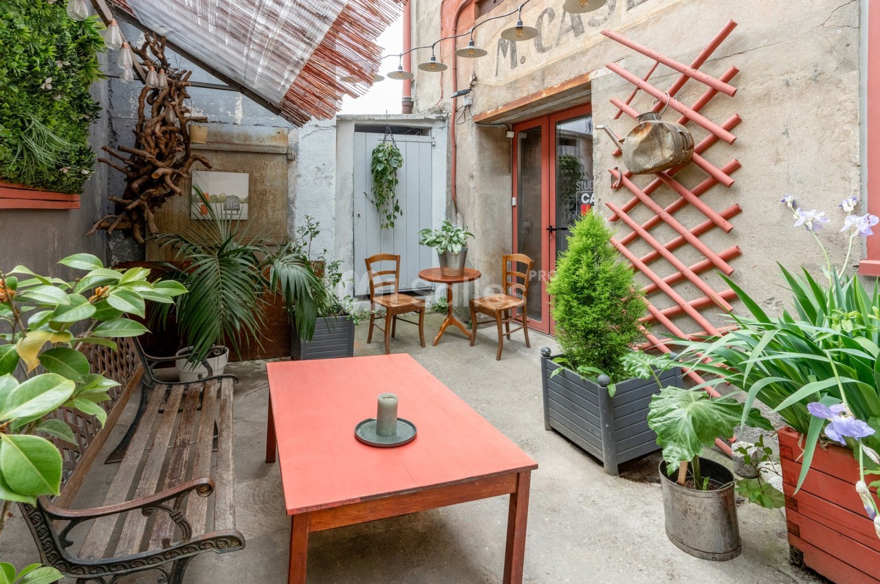 Cour intérieure aménagée avec des plantes, une table rouge, des chaises en bois et une ambiance chaleureuse.
