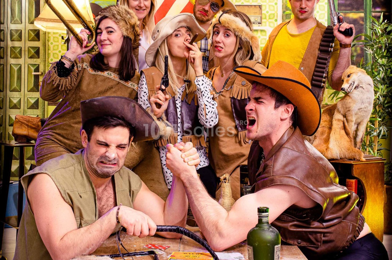Un groupe déguisé en cowboys et cowgirls dans un décor western, deux hommes font un bras de fer au premier plan.