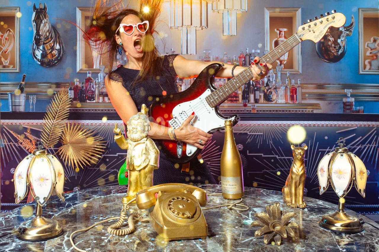 Femme jouant de la guitare électrique dans un décor rétro avec des objets dorés et un téléphone ancien sur une table en…