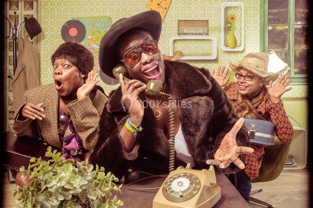 Trois personnes en tenue rétro posent de manière expressive autour d'un téléphone ancien dans un décor vintage.