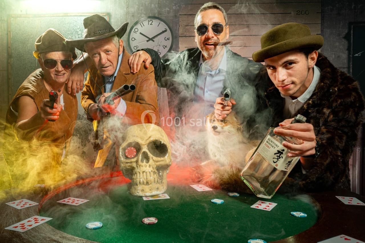Des personnes déguisées autour d'une table de poker avec un crâne, des cartes, des pistolets et une bouteille.